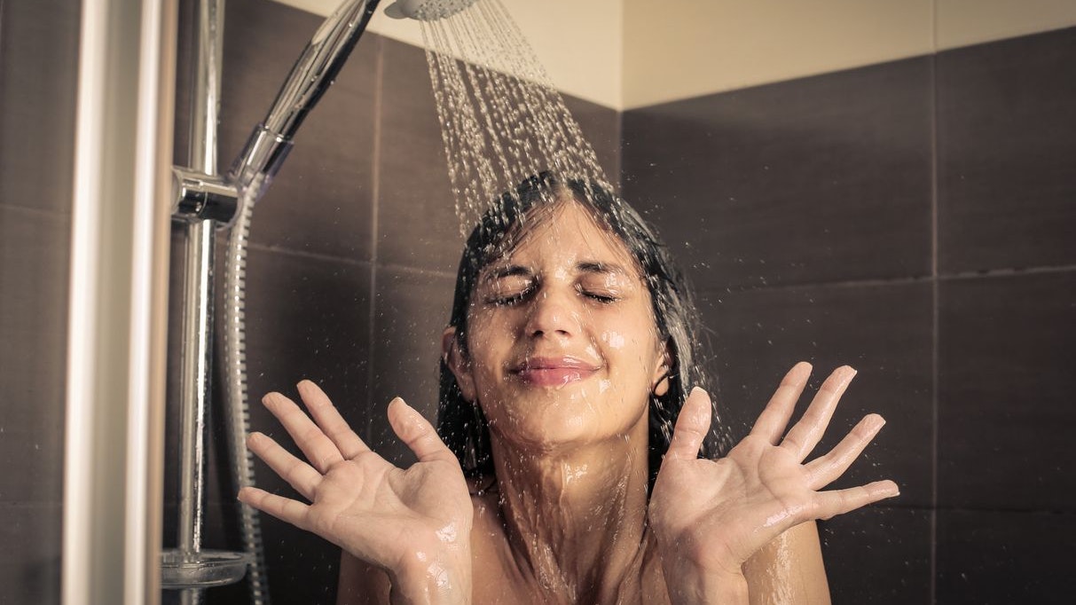 Portrait of a girl who is standing under the shower and making a funny face because the water is cold