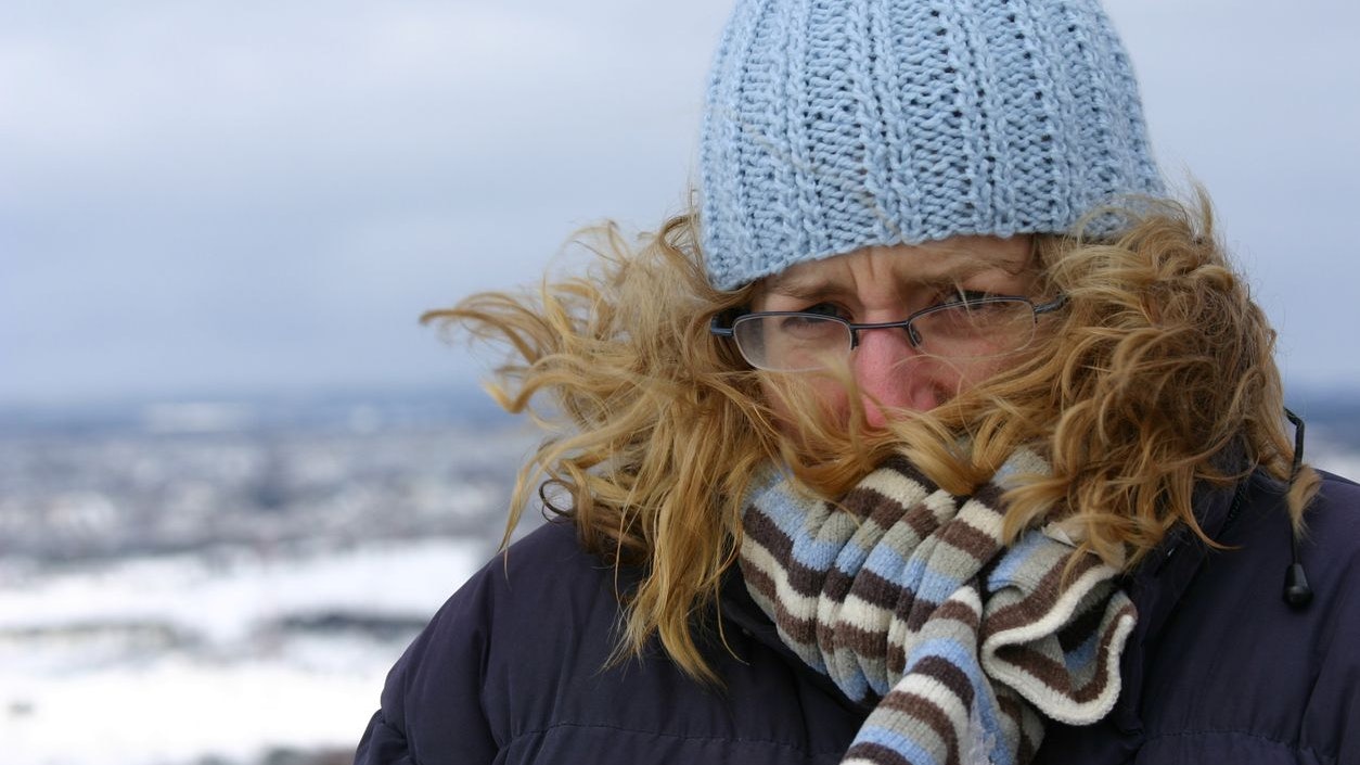 young woman bundled up sheltering from the cold wind
