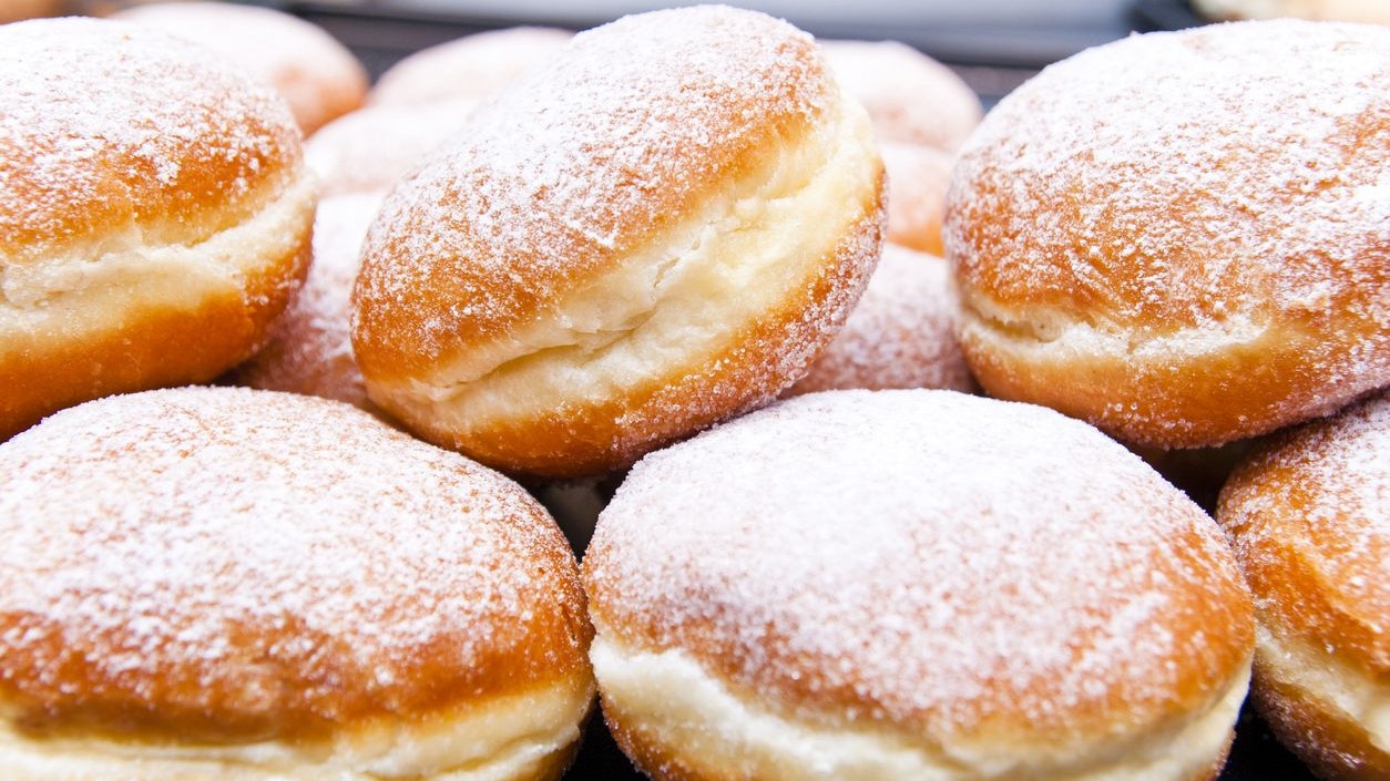 Close up a fresh German jelly doughnuts filled with raspberry jam, and decorated with fine sugar, in a retail display of a bakery. This image is part of a bakery series.