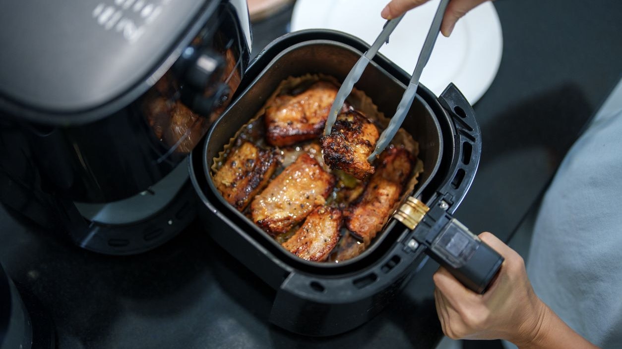 Freshly grilled pork belly with a golden-brown, crispy exterior cooked in an air fryer. The sizzling meat is being picked up with tongs, highlighting a home-cooked meal with rich seasoning.