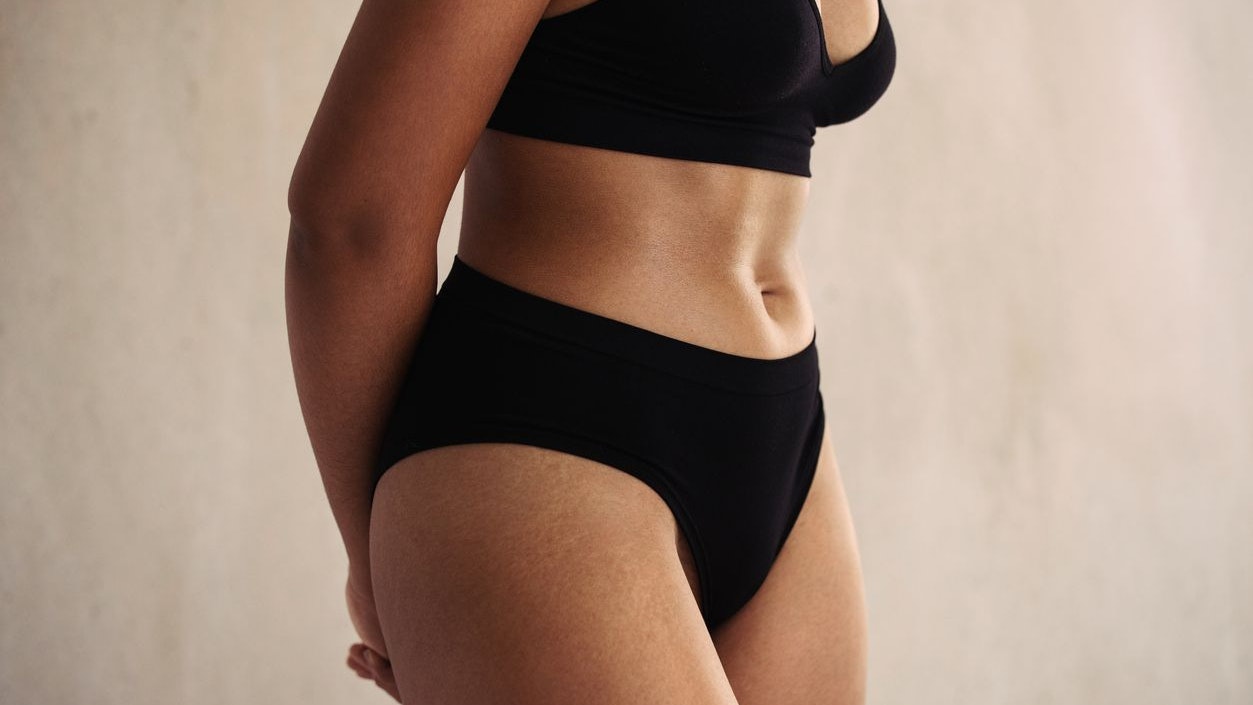 Closeup of an anonymous natural female body wearing black underwear. Young body positive woman embracing her natural body while standing alone against a studio background.