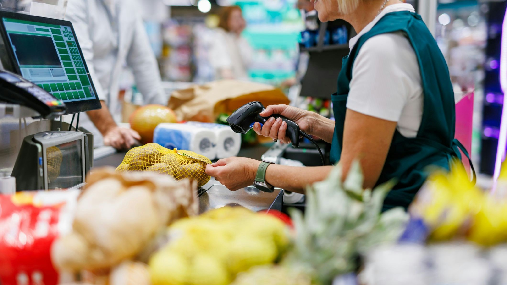 Supermarket cashier scanning groceries at the checkout with barcode reader while customer is waiting, cashier and clients are not recognizable