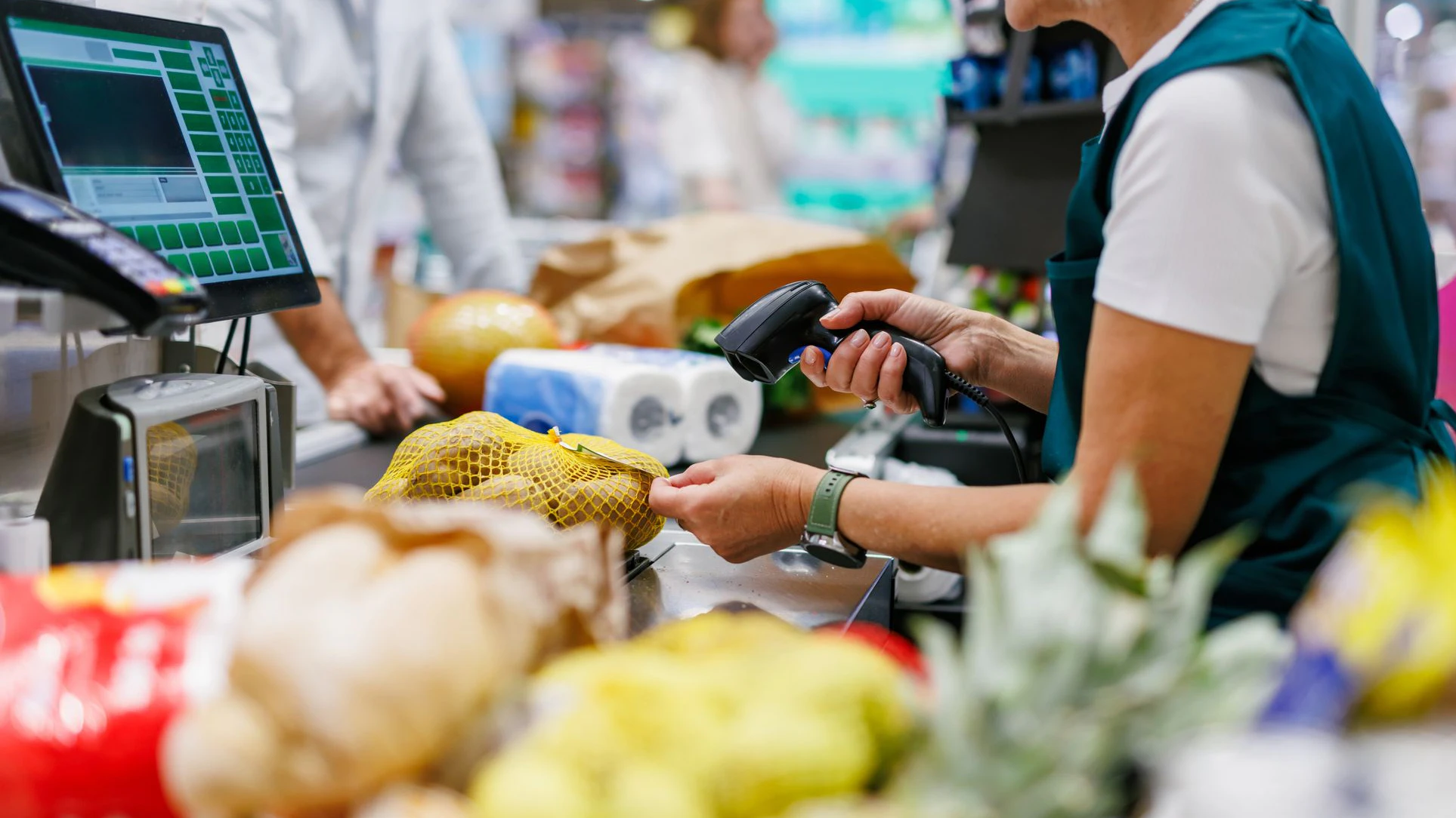 Supermarket cashier scanning groceries at the checkout with barcode reader while customer is waiting, cashier and clients are not recognizable