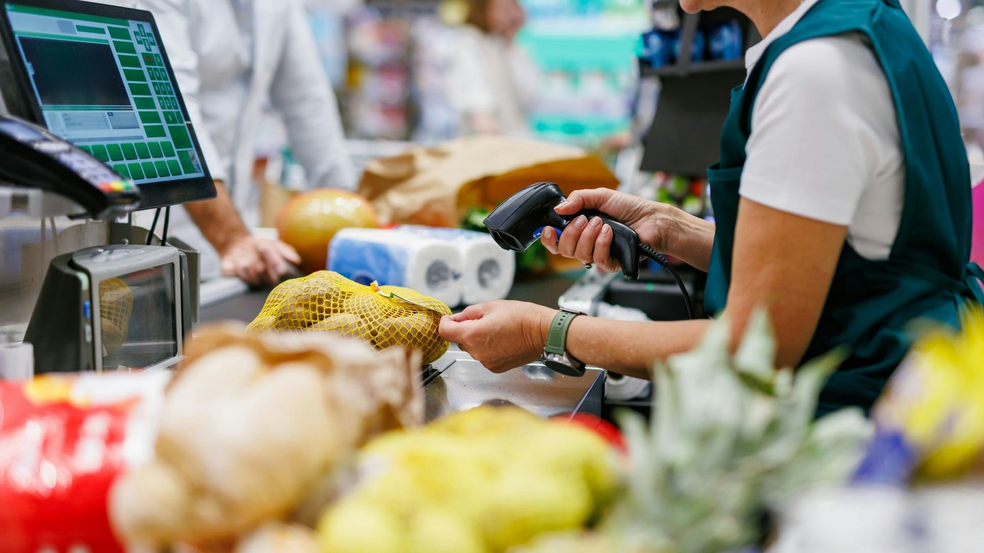 Supermarket cashier scanning groceries at the checkout with barcode reader while customer is waiting, cashier and clients are not recognizable