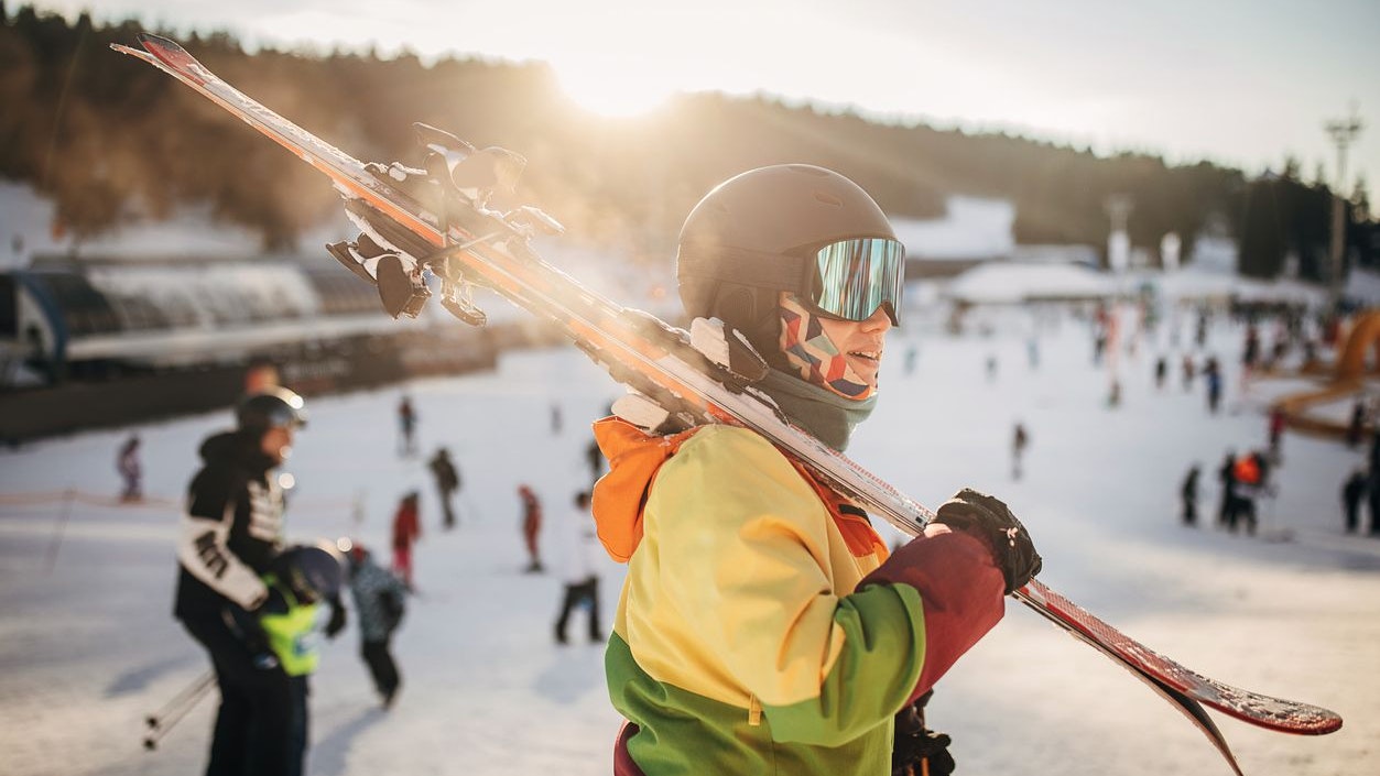 Female skier standing on a hill and carrying her skies on a snowcapped mountain ski resort.
