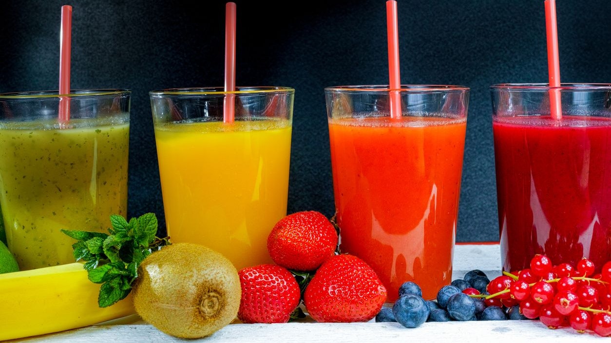 Colorful fresh pressed fruit green, yellow, oragne and red juices with fresh fruits and berries on black and red background