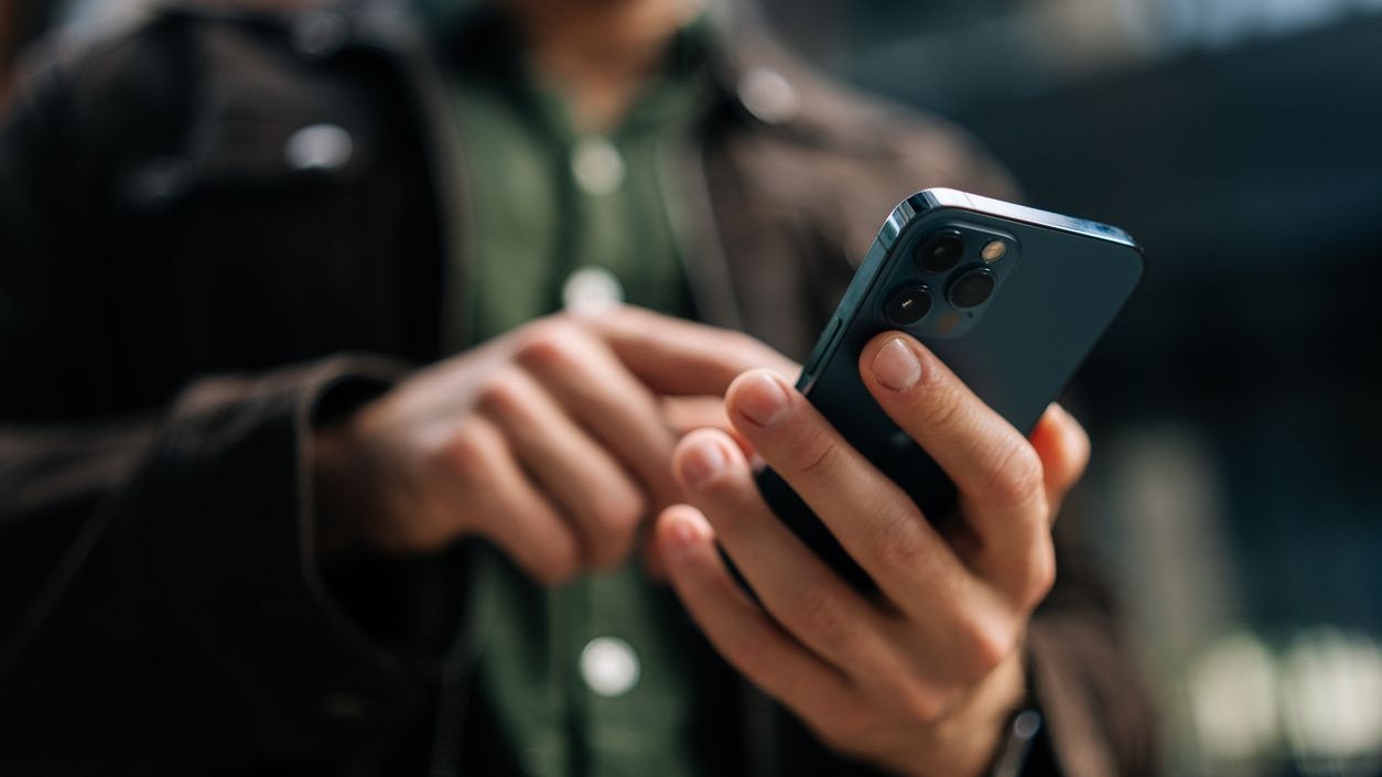 Close-up hands of unrecognizable man holding and using smartphone standing on city street, browsing internet, checking social media, using mobile application. Concept of modern communication.