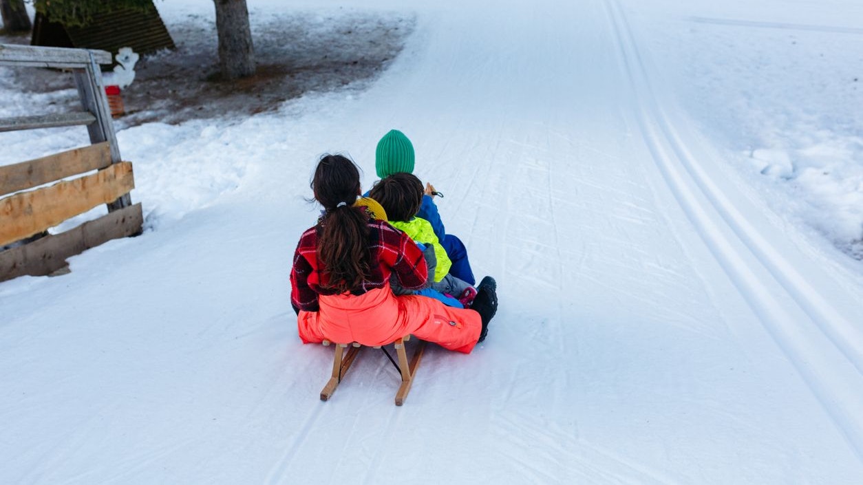 group of children in bright winter clothes riding one wooden sled going down snow slope