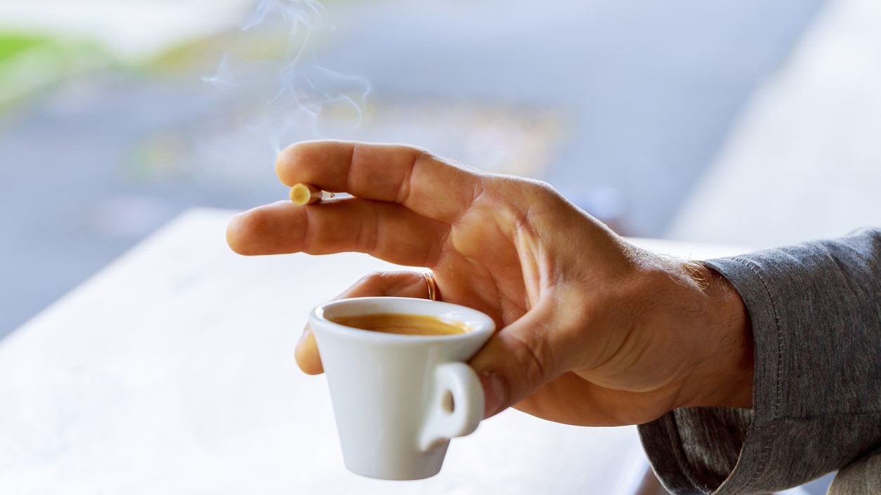 Cigarette in Male Hand With a Cup of Coffee. Smoking Addiction Concept.