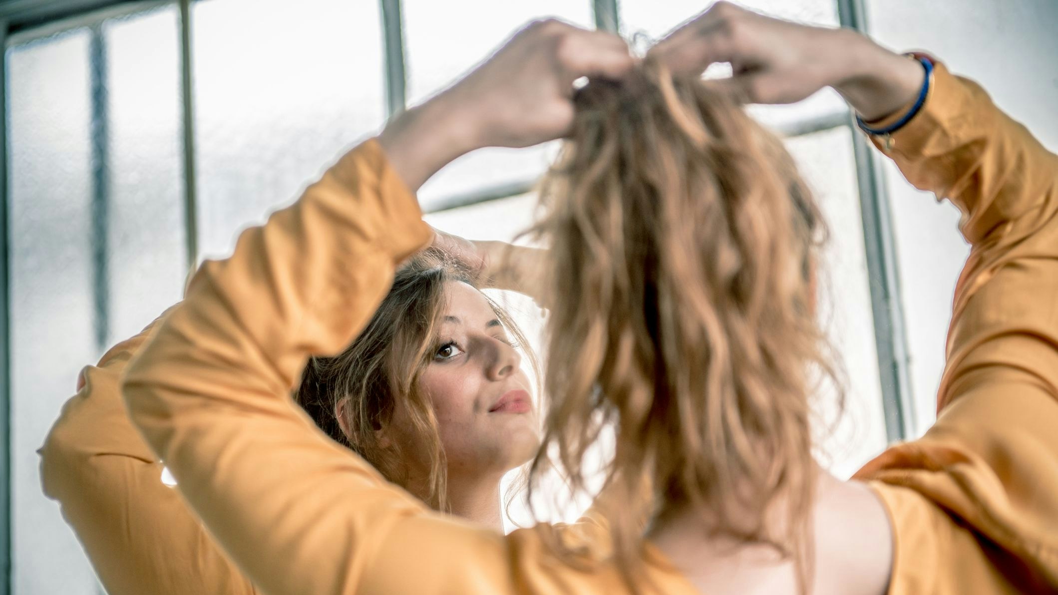 Portrait of a woman with long red hair in a ponytail looking at herself in a mirror, Paris, France. Nikon D800, full frame, XXXL. iStockaLypse Paris 2016.
