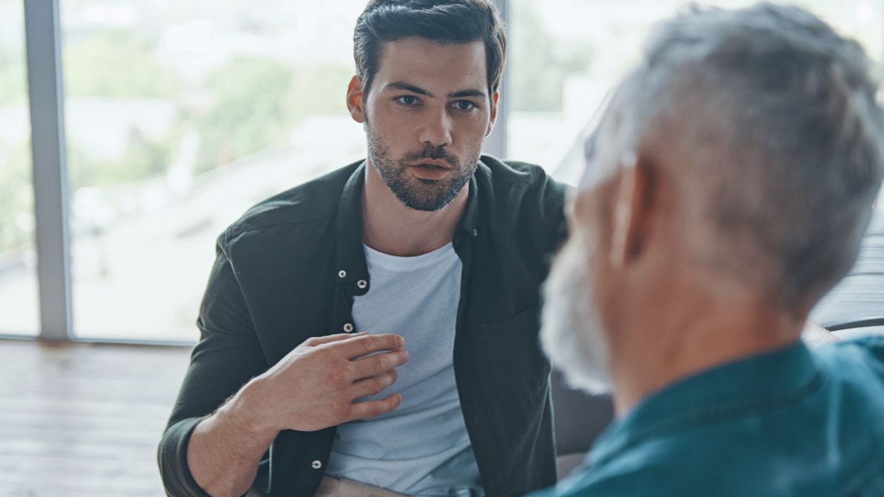 Handsome young man talking to his senior father while spending time at home together
