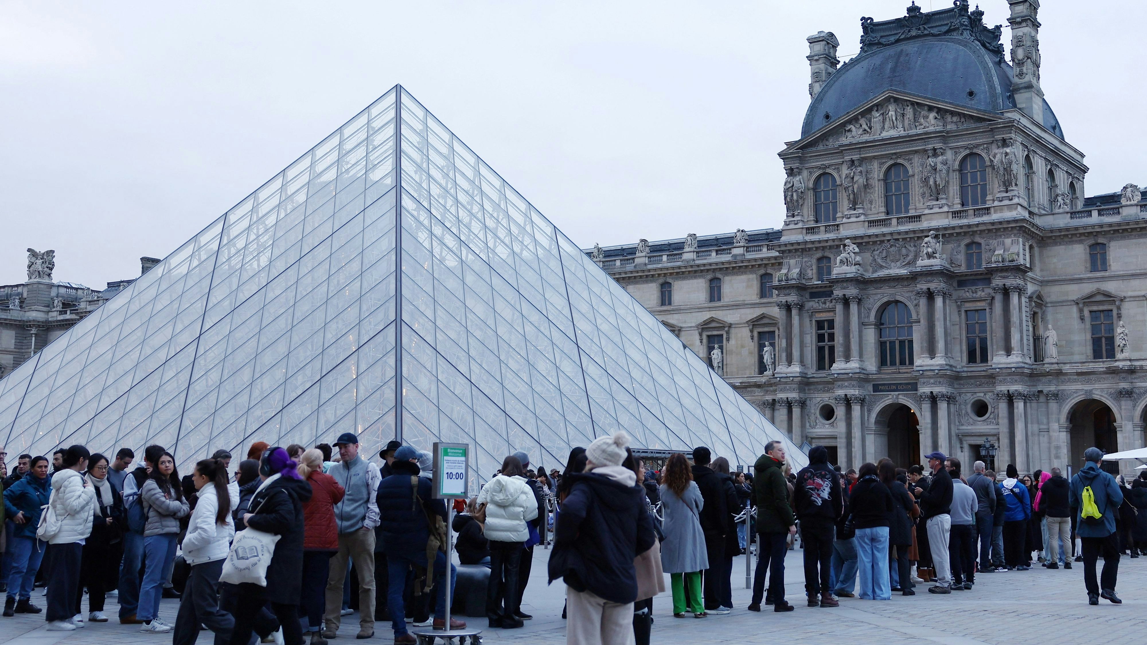 People stand near the glass Pyramid of the Louvre Museum which remains closed as its staff continue discussions on whether to extend a strike over pay and working conditions at the museum, the state of the museum's buildings and staffing issues, two months after a spectacular heist which saw thieves make off with jewels in broad daylight, in Paris, France, December 17, 2025. REUTERS/Abdul Saboor