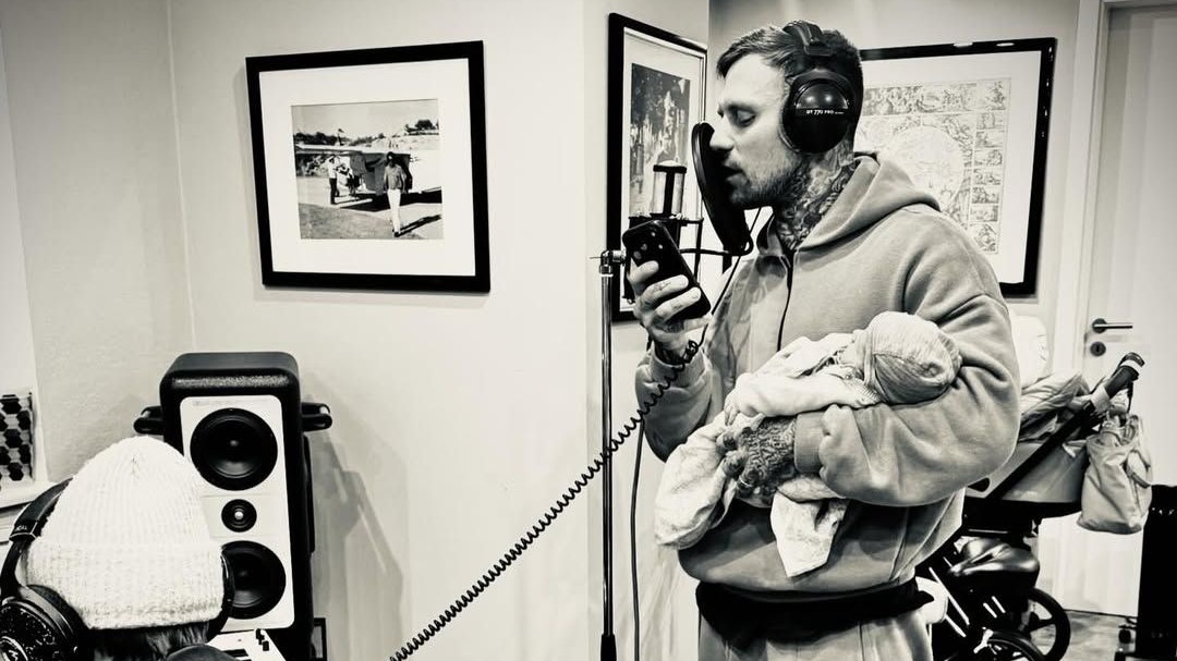 Kontra K hält sein Neugeborenes während einer Aufnahme im Arm.