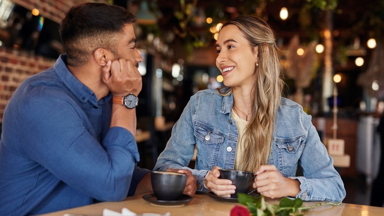 Coffee shop, date and couple of friends with rose for valentines day, anniversary or love in restaurant bokeh. Happy diversity people or woman with love partner at cafe at night for social talking