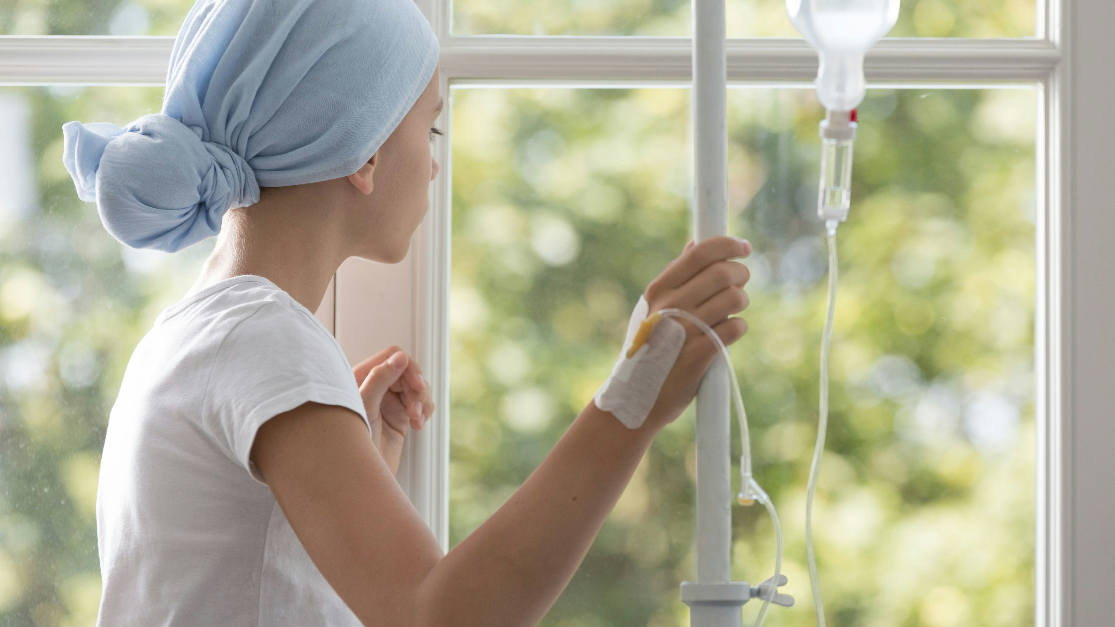 Sick child with drip wearing blue headscarf during treatment in the hospital
