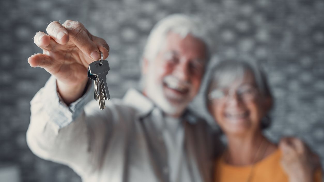 Close up focus of happy old Caucasian couple show keys to own apartment or house. Smiling mature retired man and woman celebrate relocation to new home. Moving, rental, estate concept.