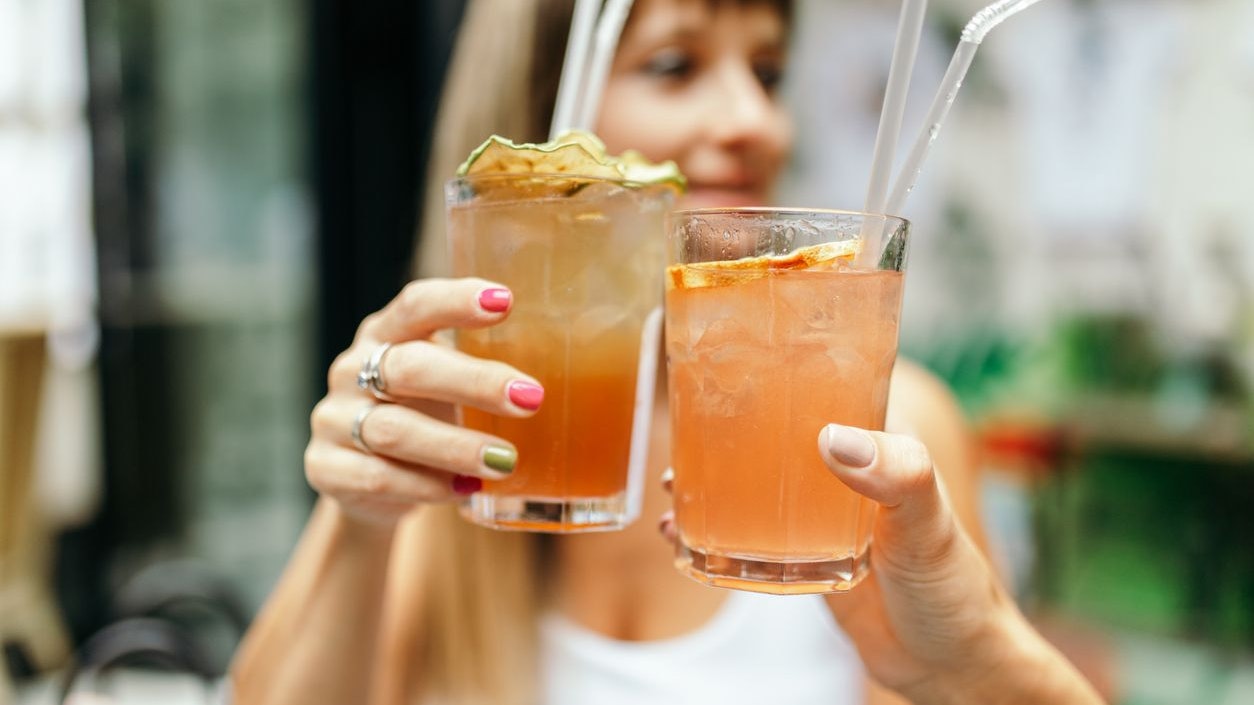 Two female friends, two young women sitting in cafe bar at daytime and having fun and laughing a lot while drinking cocktails and cheering