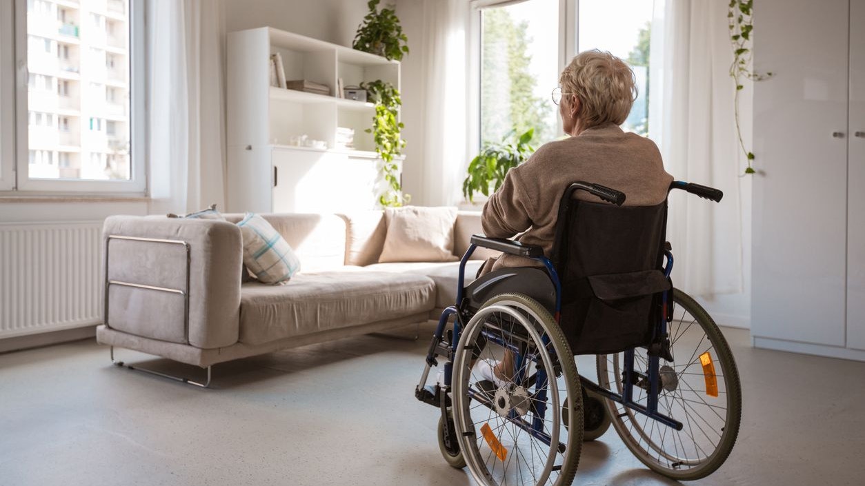 Back view of lonely senior woman sitting in a wheelchair in her room.