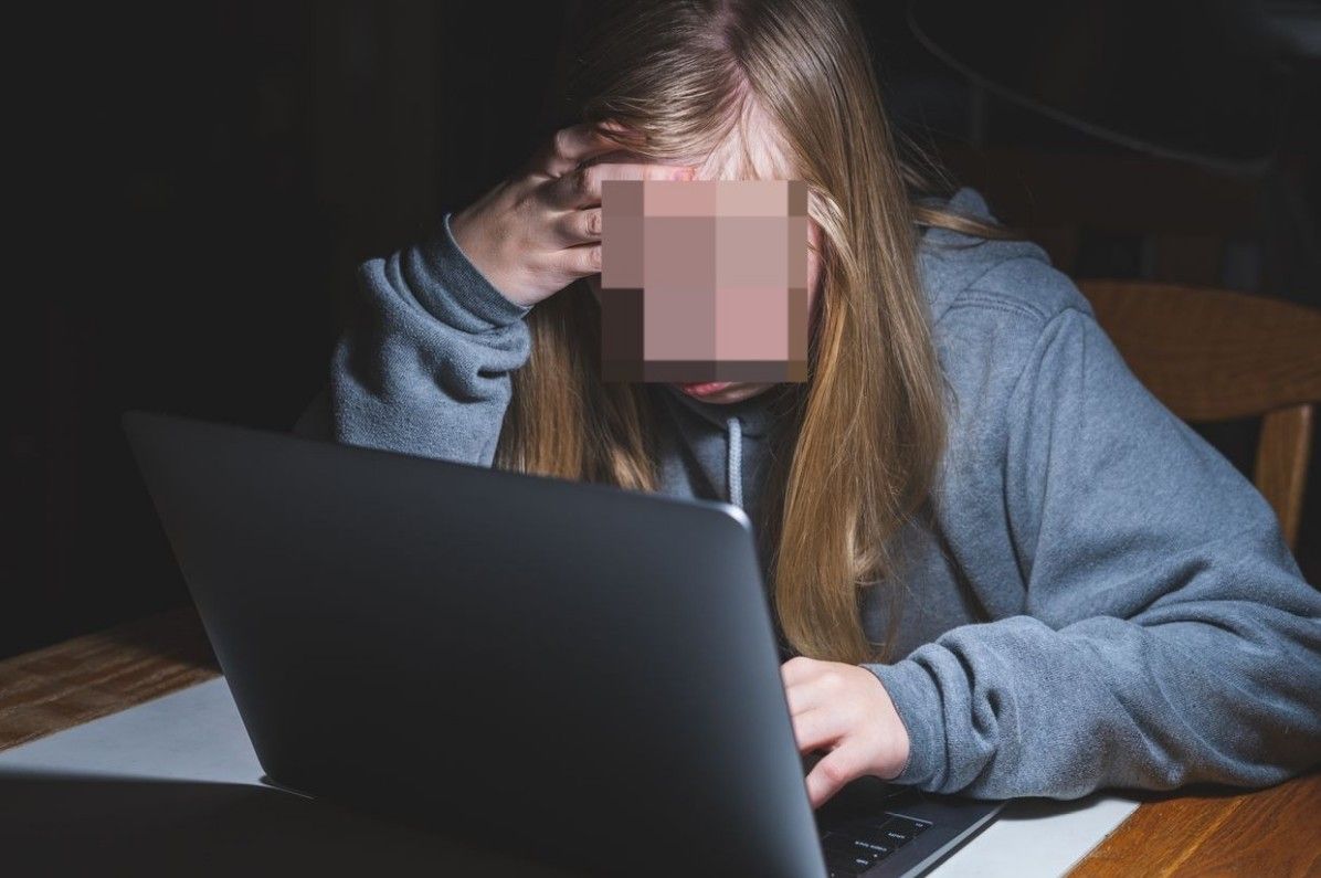Eine Schülerin sitzt verzweifelt vor ihrem Laptop, nachdem manipulierte KI-Bilder von ihr verbreitet wurden (Symbolfoto).