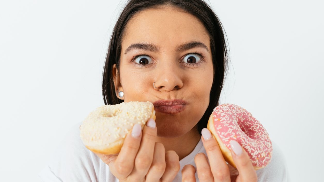Portrait of funny young happy woman eating sweets donuts, white background.