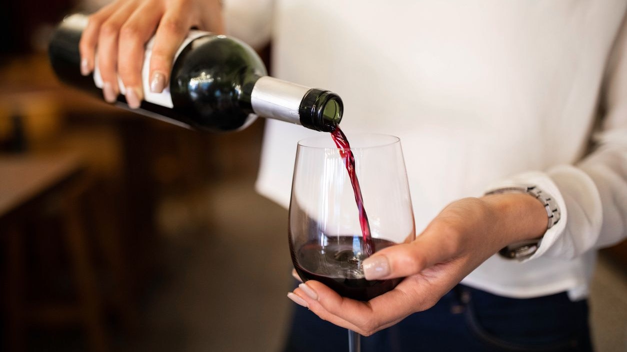Close-up of a woman hand pouring wine into a glass. Female waiter serving red wine in a winery.