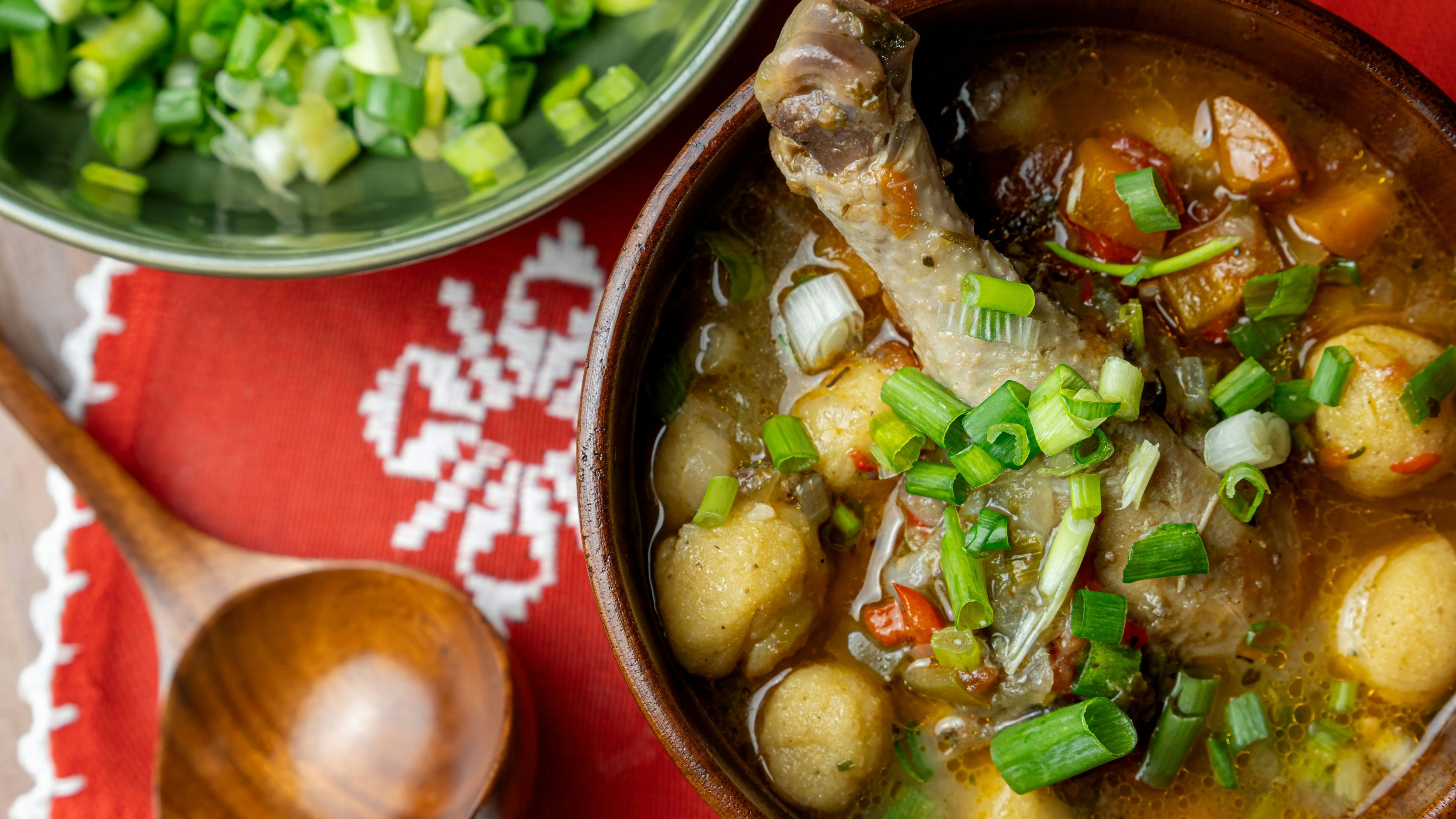 Authentic Vori Vori soup with chicken, vori vori balls, and vegetables in rustic wooden bowl, displayed on vibrant red Aopo'i handmade lace, showcasing traditional Paraguayan culinary heritage.