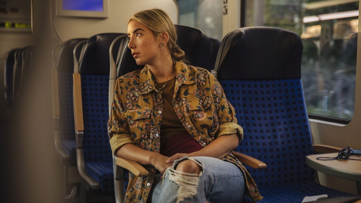 A young woman enjoys the train ride while looking out the window.