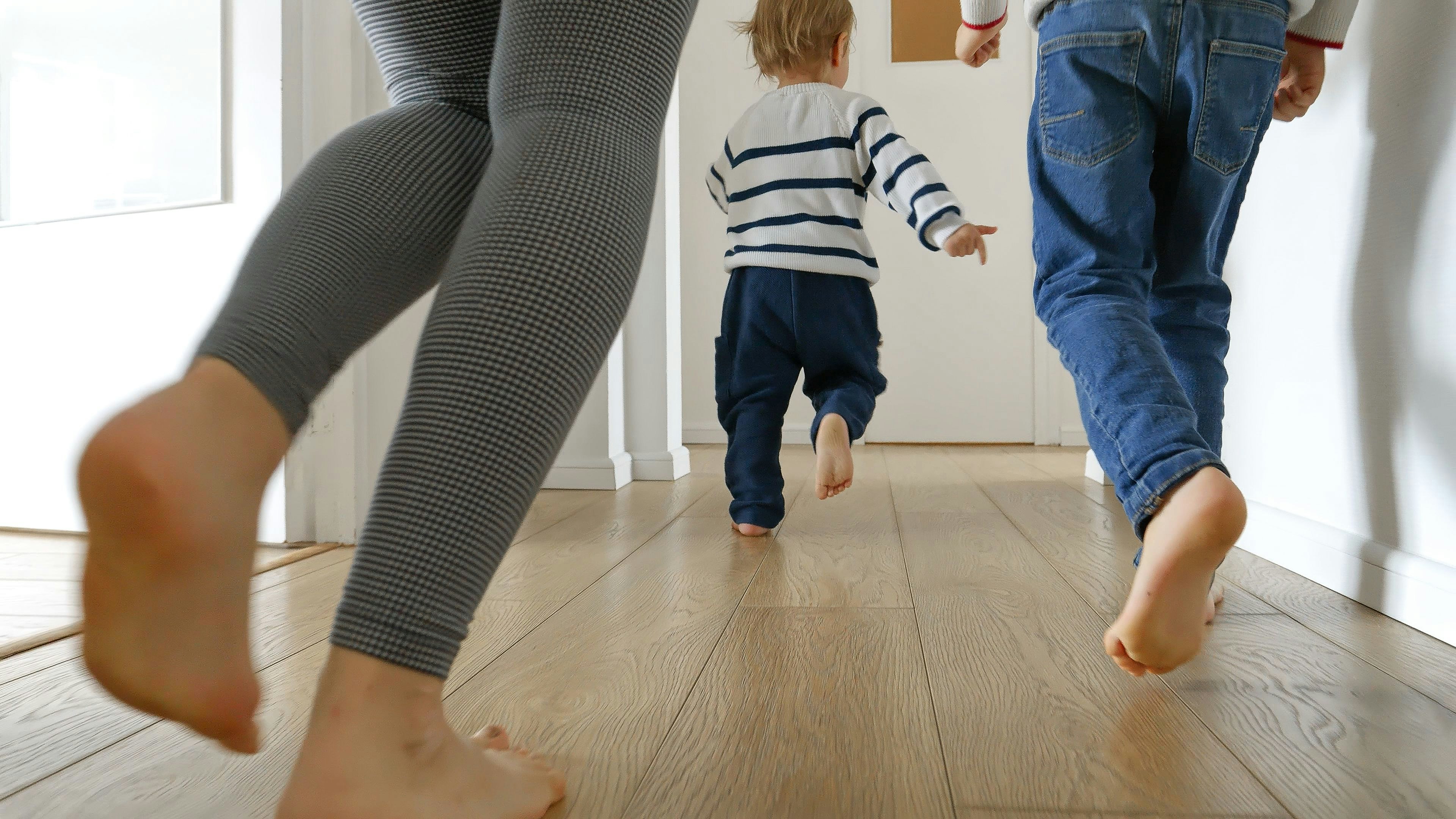 Closeup of mother and two boys running on the wooden floor at home. Concept of family love, joy, and fun in a household.