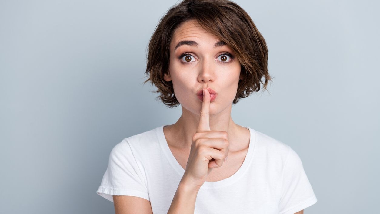 Photo of adorable girlish tricky woman with bob hairstyle dressed white t-shirt hold finger on lips isolated on gray color background.