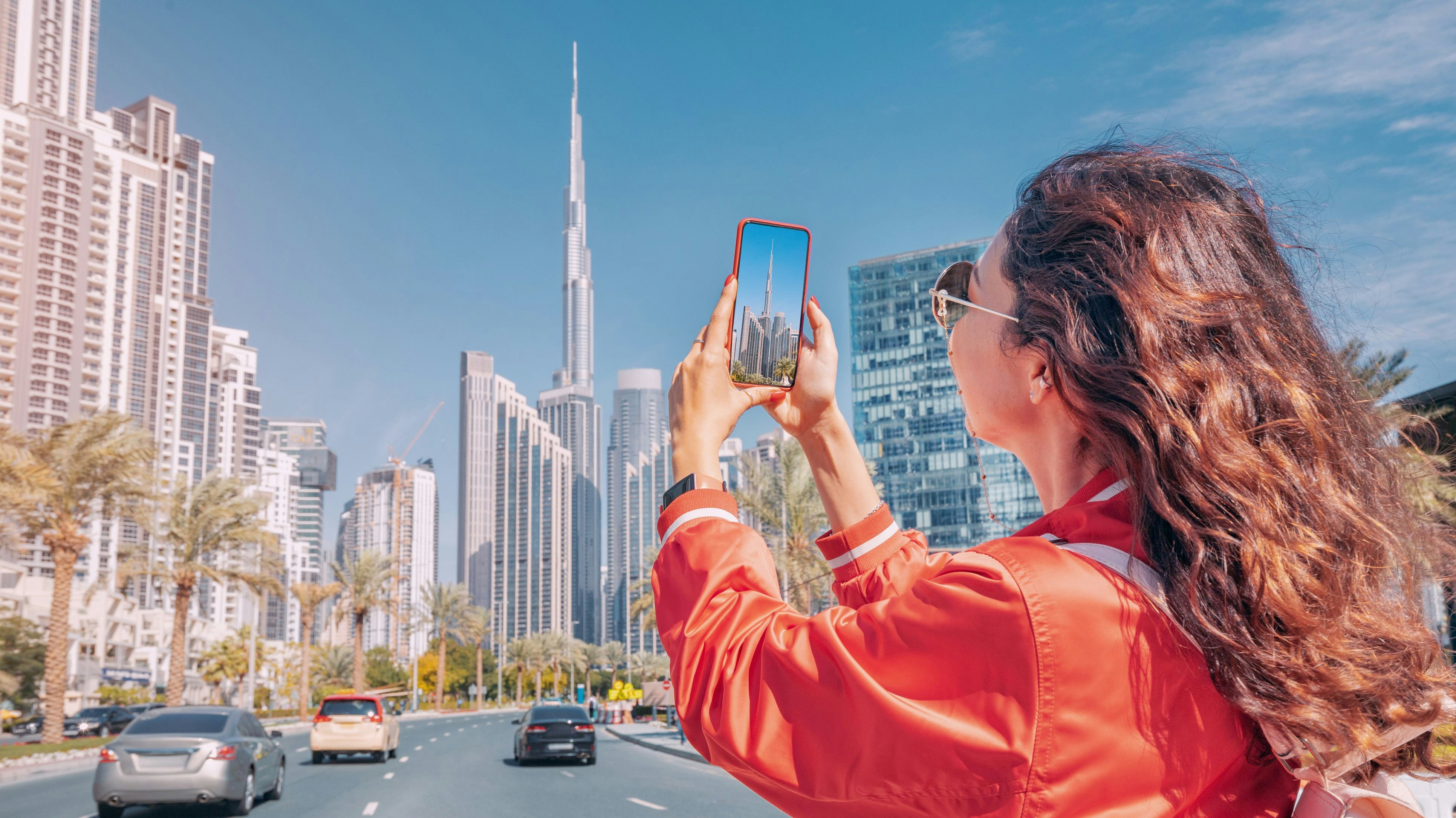 Tourist happy girl taking photos for her travel blog, in Dubai downtown district against background of the Burj Khalifa highest skyscraper