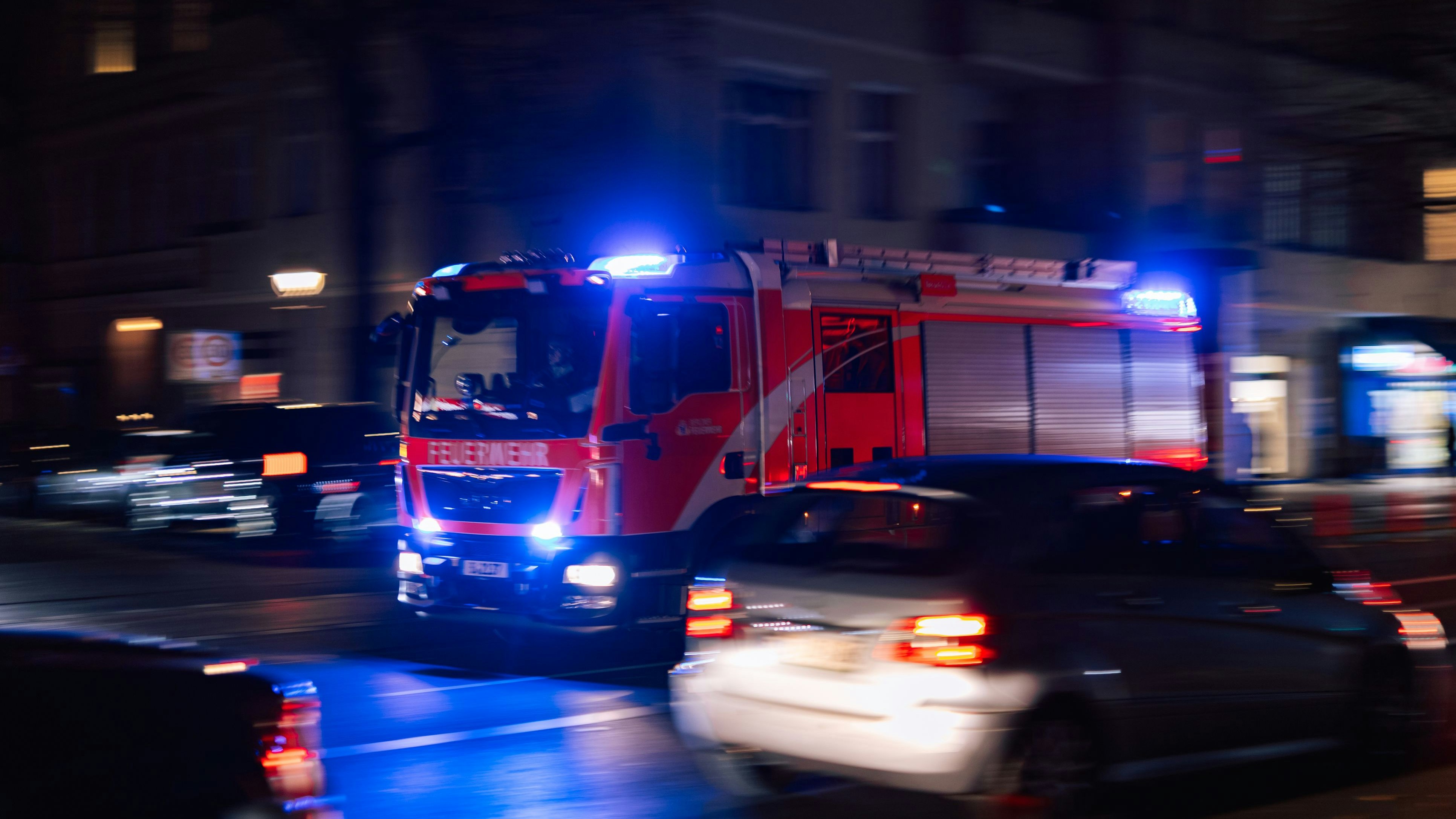 Berlin, Germany – October 16, 2025: Fire truck with flashing blue lights moves through a Berlin street at night. Other cars are visible on the road in motion blur.