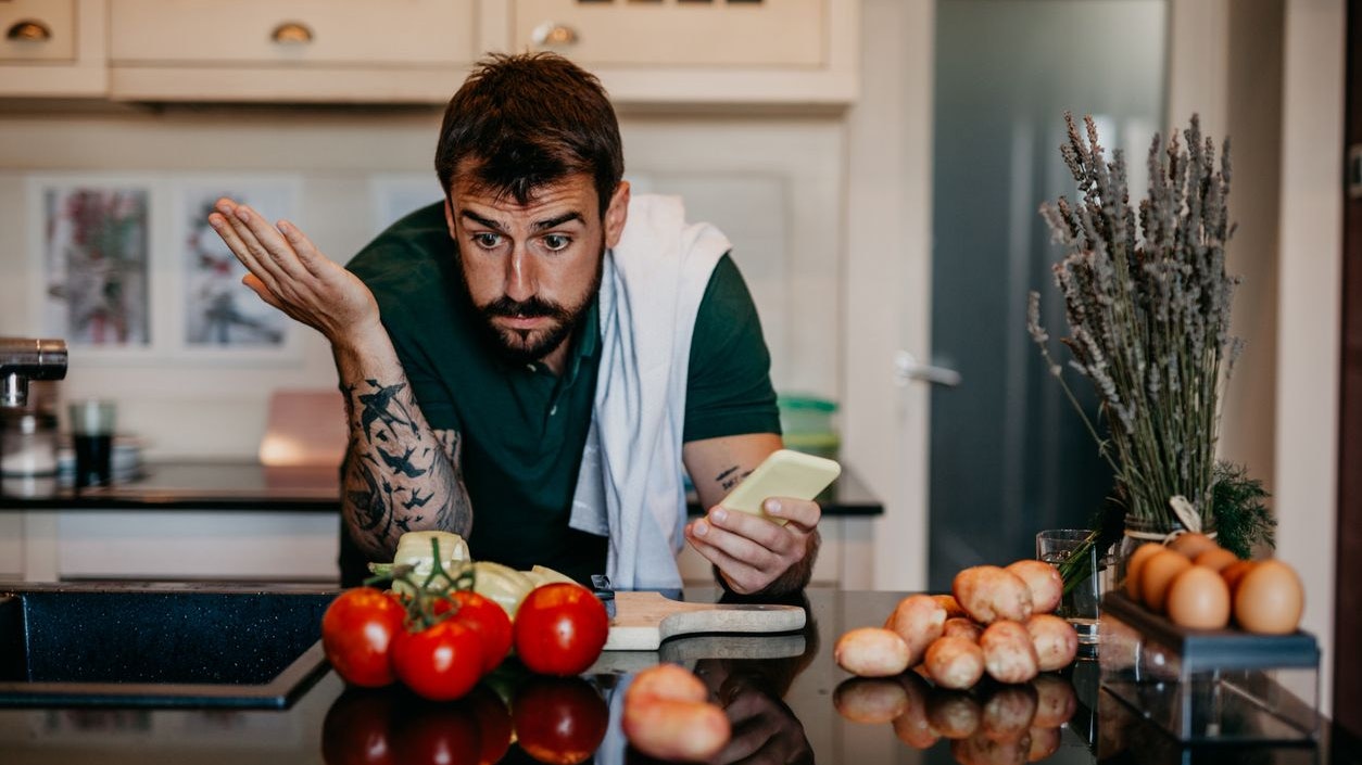 Bearded man in the kitchen, using a smartphone as a cooking recipe, ready to make some lunch at home.