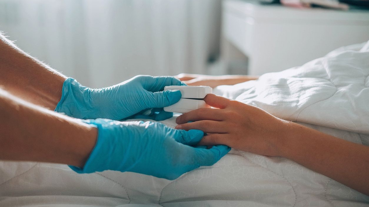 The child lies in bed, a doctor in medical gloves comes up to him and puts a pulse oximeter on his finger to measure the oxygen saturation. Asthma treatment.  Bedroom or hospital room for young patien