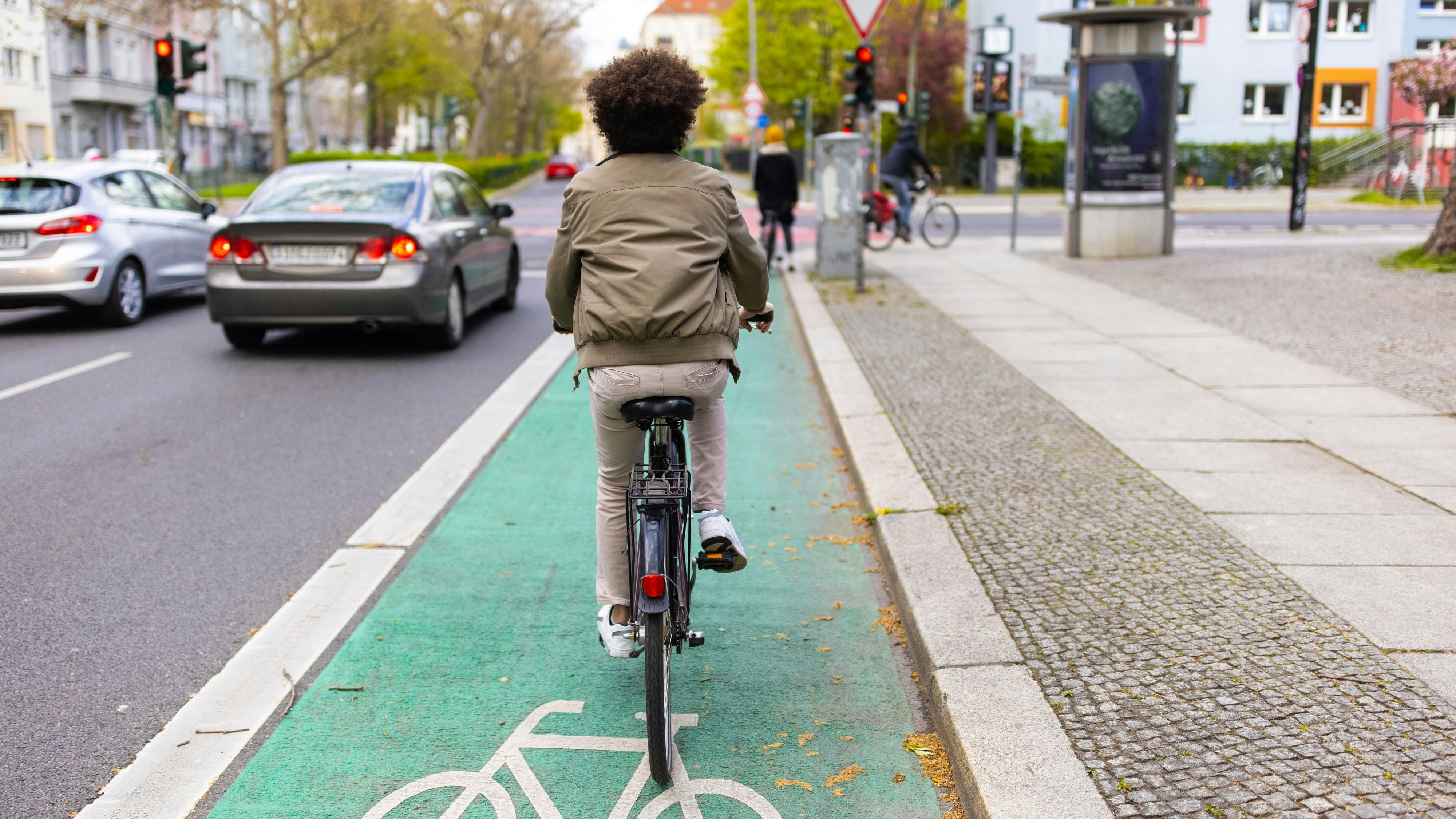 Rear view of a man riding his cycle on green colored bicycle lane. Male cyclist commuting in city traffic.