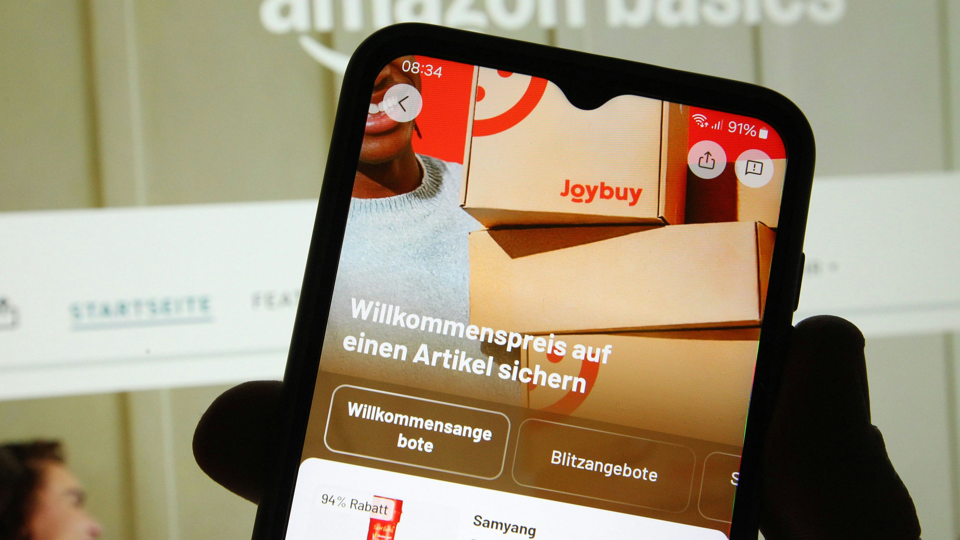 Auf einem Laptop wurde die Website von Amazon mit den Angeboten von AmazonBasics geöffnet. Davor wurde auf einem Smartphone die App des chinesischen Konkurrenten den US-Unternehmens Joybuy geöffnet. Symbolbild/Symbolfoto. Schnelsen Hamburg *** The Amazon website with the AmazonBasics offers was opened on a laptop Before that, the app of the Chinese competitor, the US company Joybuy, was opened on a smartphone Symbol image Symbol photo Schnelsen Hamburg