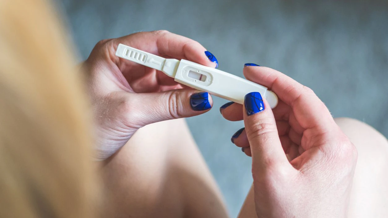 Young blonde girl sitting and looking at a negative pregnancy test, top view