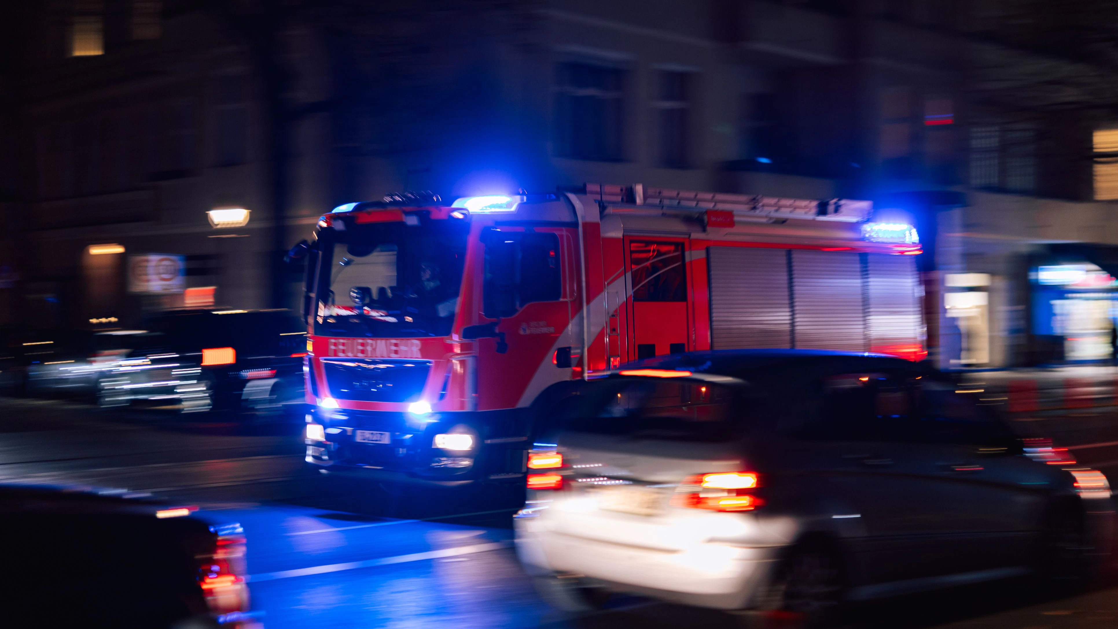 Berlin, Germany – October 16, 2025: Fire truck with flashing blue lights moves through a Berlin street at night. Other cars are visible on the road in motion blur.