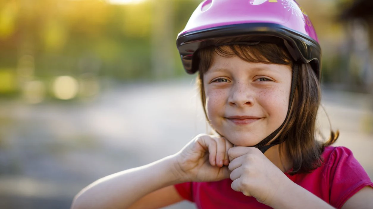 Happy cute girl putting cycle helmet on