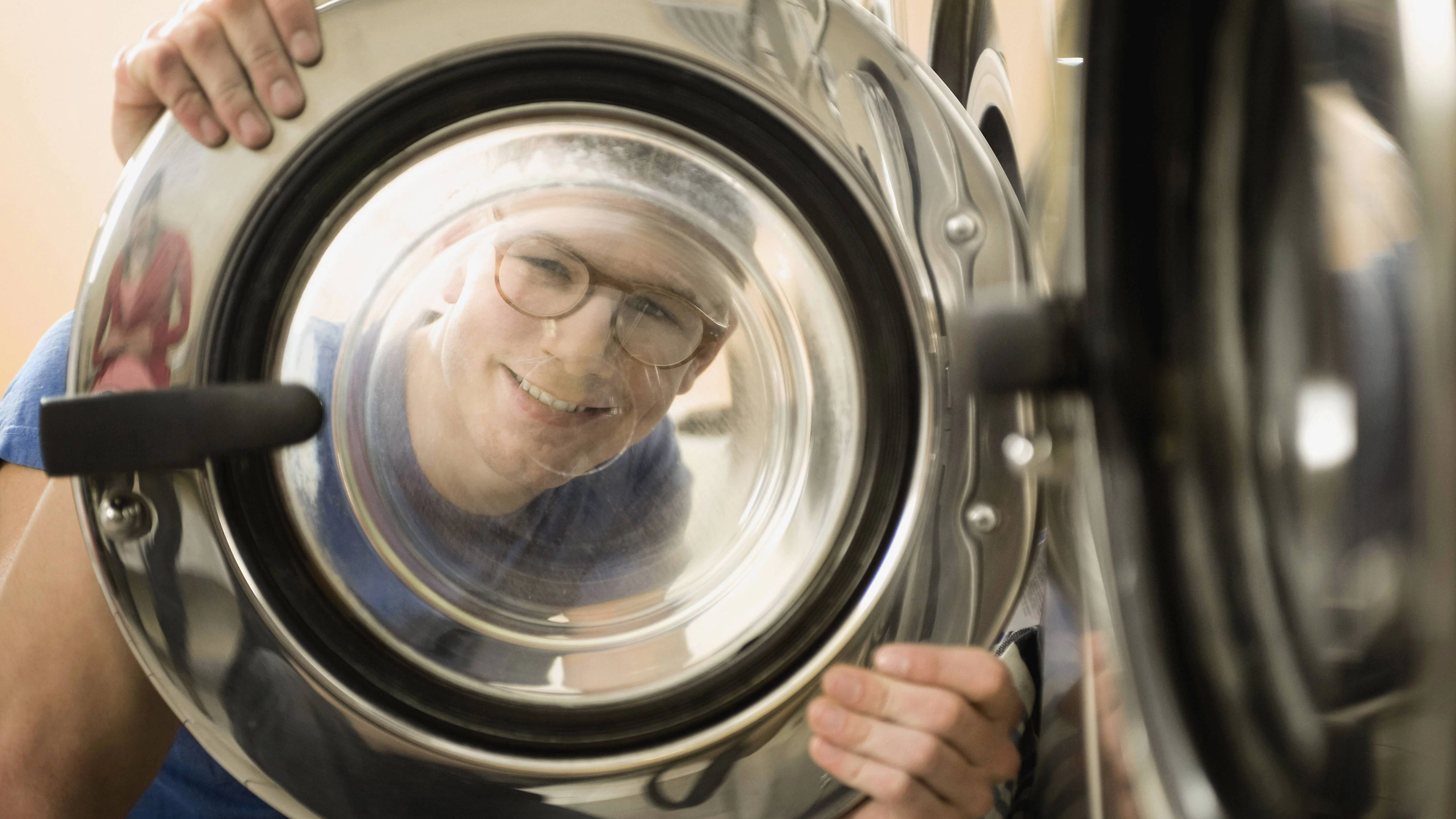 Young man looking through window of washing machine, smiling mit_2003_00366  