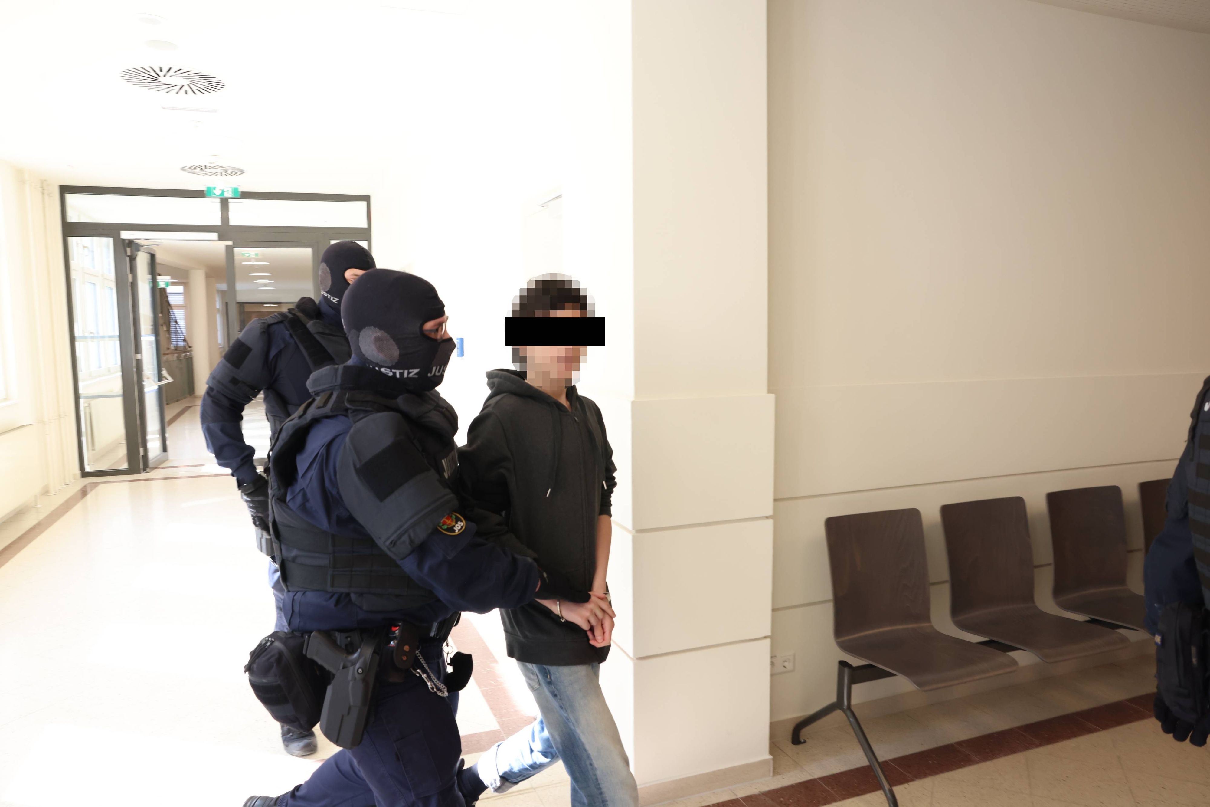 Maskierte Justizwache führt den 15-Jährigen in den Gerichtssaal.