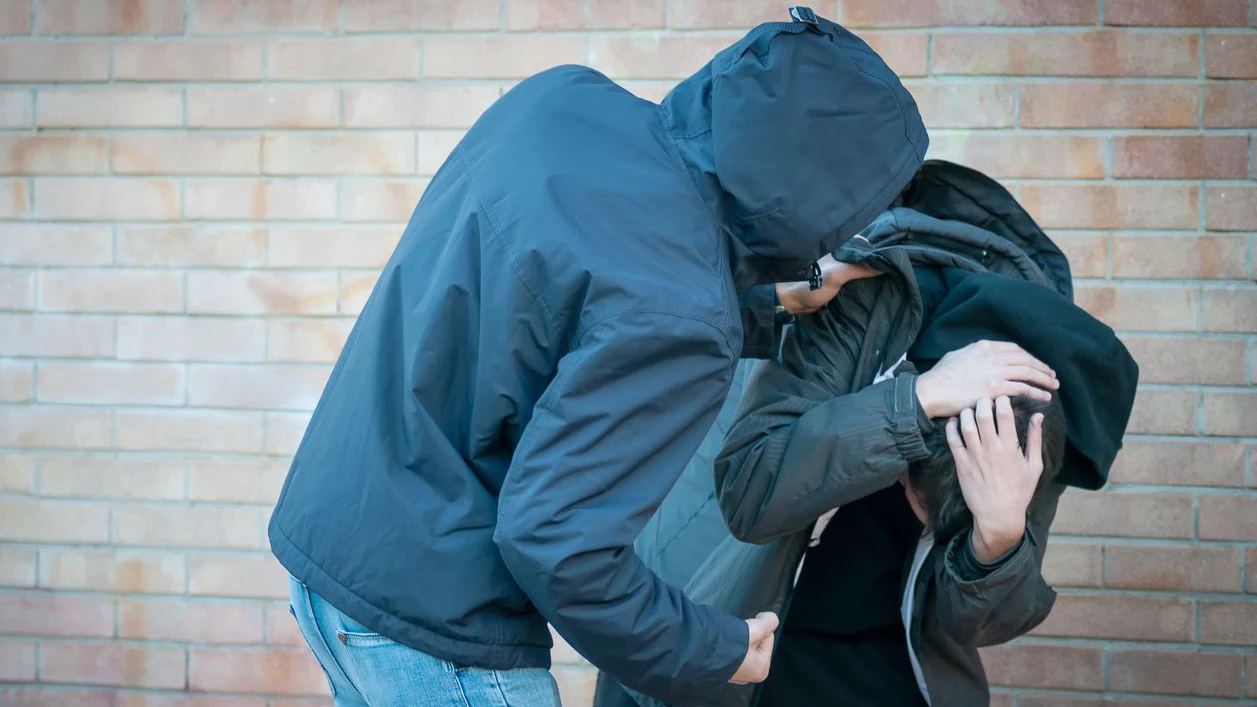 Bullying, aggression and violence scene between two males, one young adult male punches his peer near a bricks wall