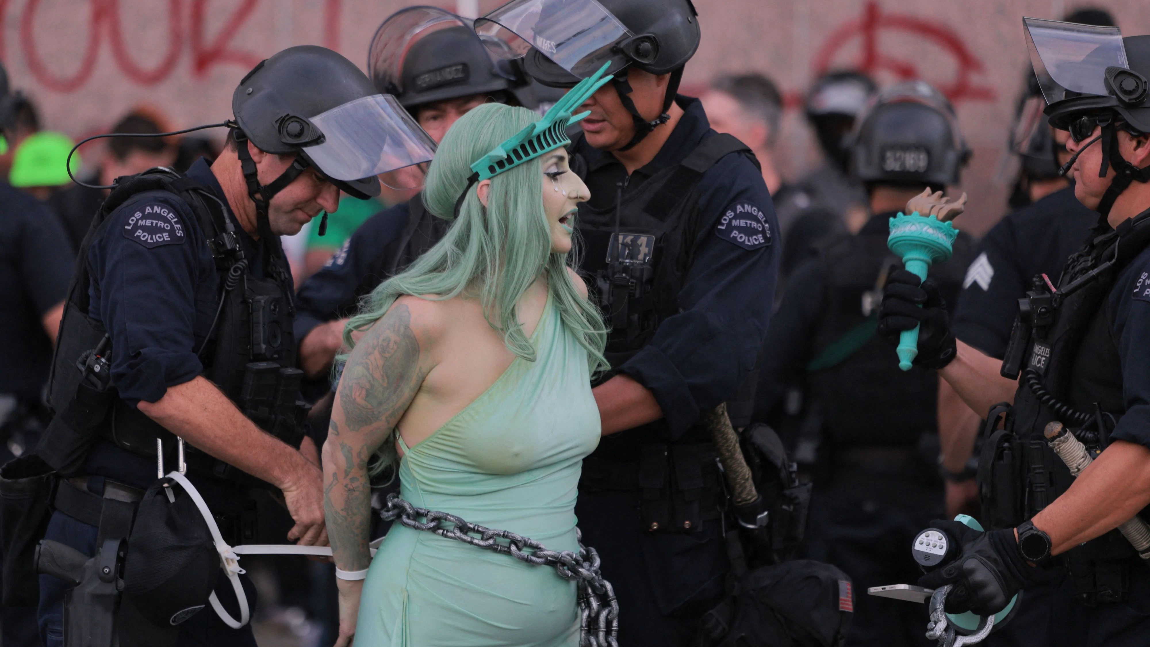 LAPD officers arrest a protester dressed as Lady Liberty in chains following clashes near the Metropolitan Detention Center during the "No Kings" national day of protest in Los Angeles on March 28, 2026. Nationwide protests against US President Donald Trump are expected Saturday as millions of people vent fury over what they see as his authoritarian bent and other forms of cruel, law-trampling governance. It is the third time in less than a year that Americans will take to the streets as part of a grassroots movement called "No Kings," the most vocal and visual conduit for opposition to Trump since he began his second term in January 2025. (Photo by Etienne LAURENT / AFP)