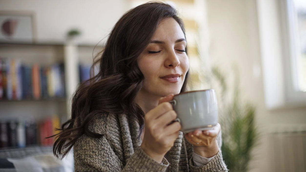 Young smiling woman enjoying in smell of fresh coffee at home