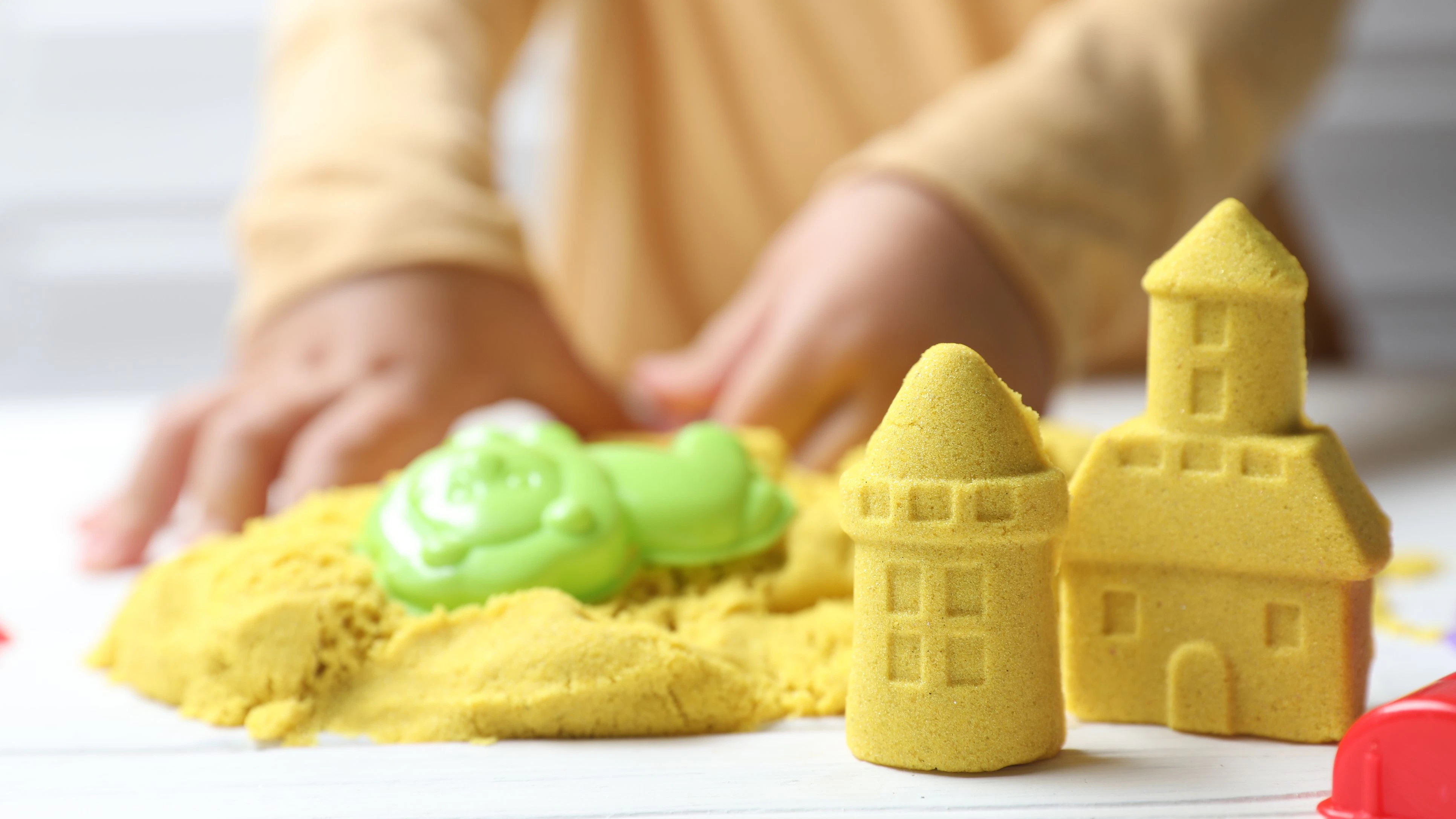 Little child playing with yellow kinetic sand at white wooden table, selective focus