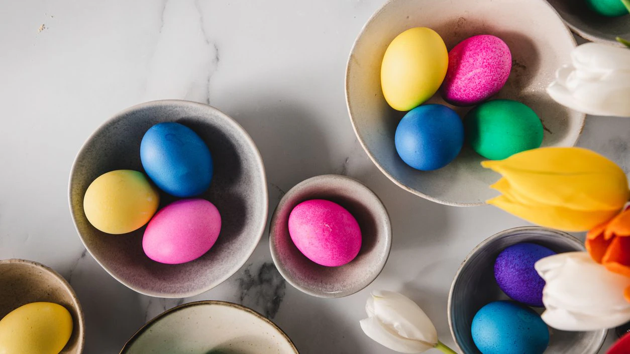 Directly above shot of colorful eggs in bowls with tulips flowers over marble surface. Easter decoration background.