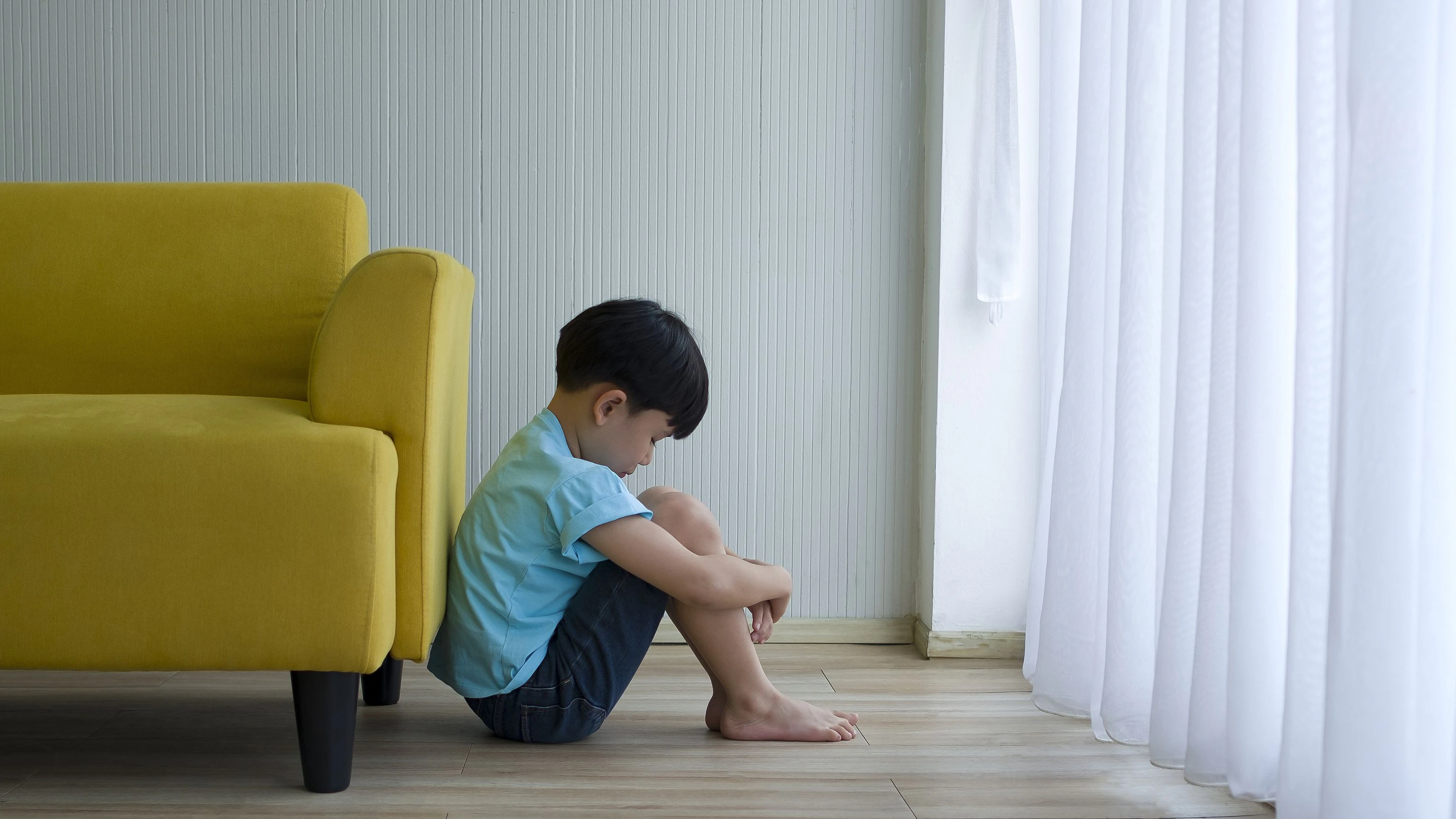 Little boy sitting beside yellow sofa at home. Child autism.