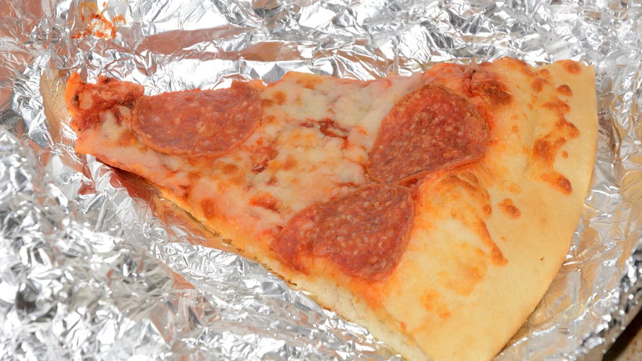 Leftovers: cold piece of pepperoni pizza on aluminum foil