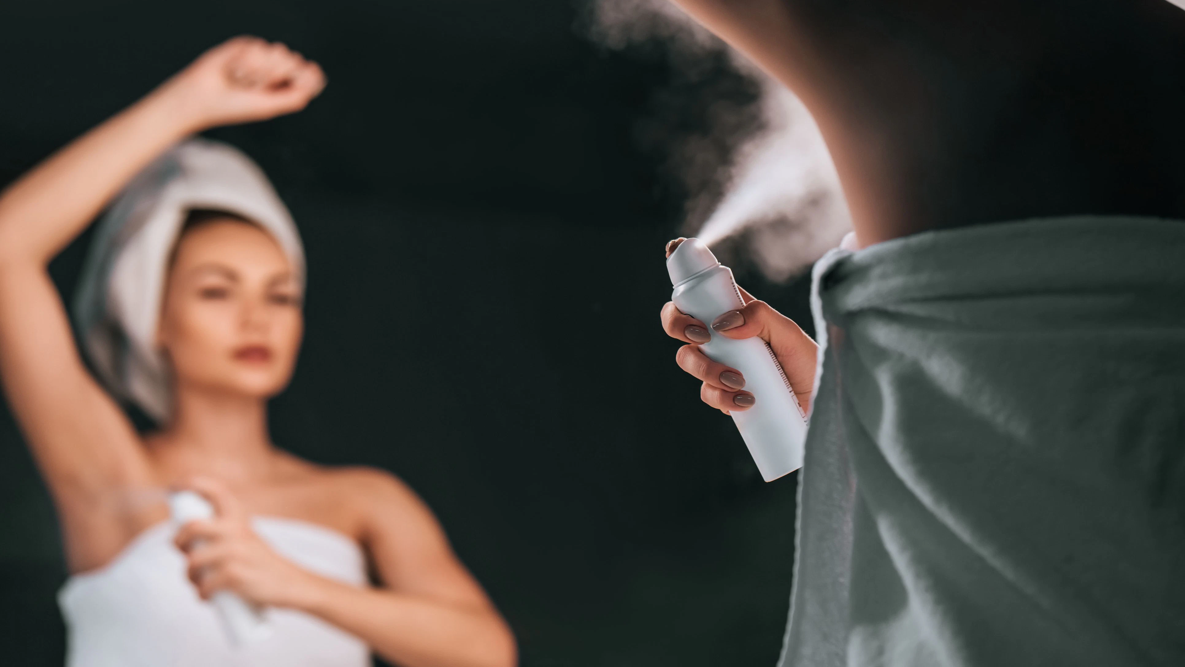 Attractive young woman in bathroom after shower is standing in front of mirror with deodorant in hands. Women care.