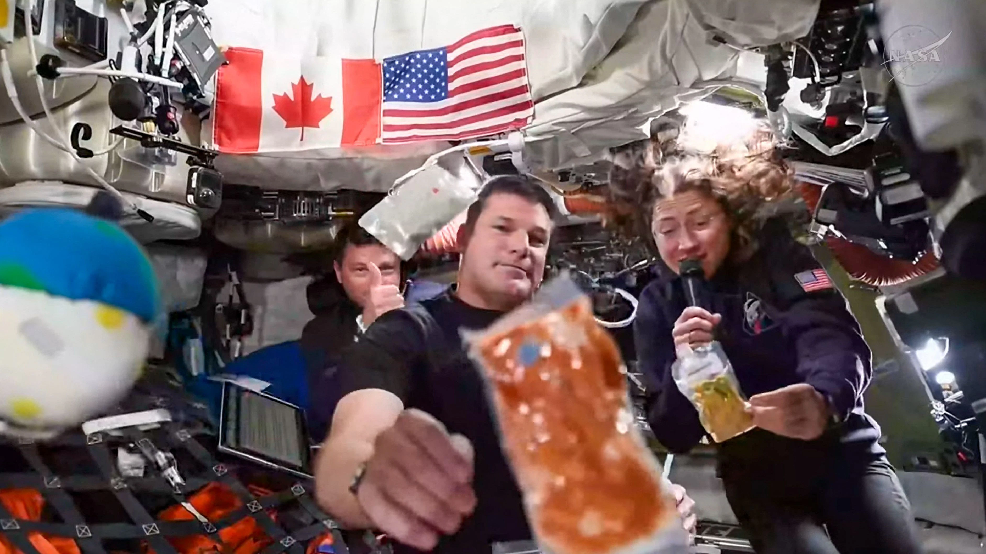 *** HANDOUT *** This screengrab taken from a NASA livestream shows Artemis II mission astronauts (L-R) NASA's commander Reid Wiseman, Canadian Space Agency's mission specialist Jeremy Hansen and NASA's mission specialist Christina Koch during a brief demonstration of the food they eat in space to respond a question during a "VIP call" with Canadian children inside the Orion spacecraft while on their way to the Moon on April 4, 2026. The four astronauts for the Artemis II mission were gearing up April 4 for their long-anticipated lunar flyby, including reviewing the surface features they must analyze and photograph during their time circling the Moon. (Photo by Handout / NASA / AFP) / RESTRICTED TO EDITORIAL USE - MANDATORY CREDIT "AFP PHOTO / NASA" - HANDOUT - NO MARKETING NO ADVERTISING CAMPAIGNS - DISTRIBUTED AS A SERVICE TO CLIENTS