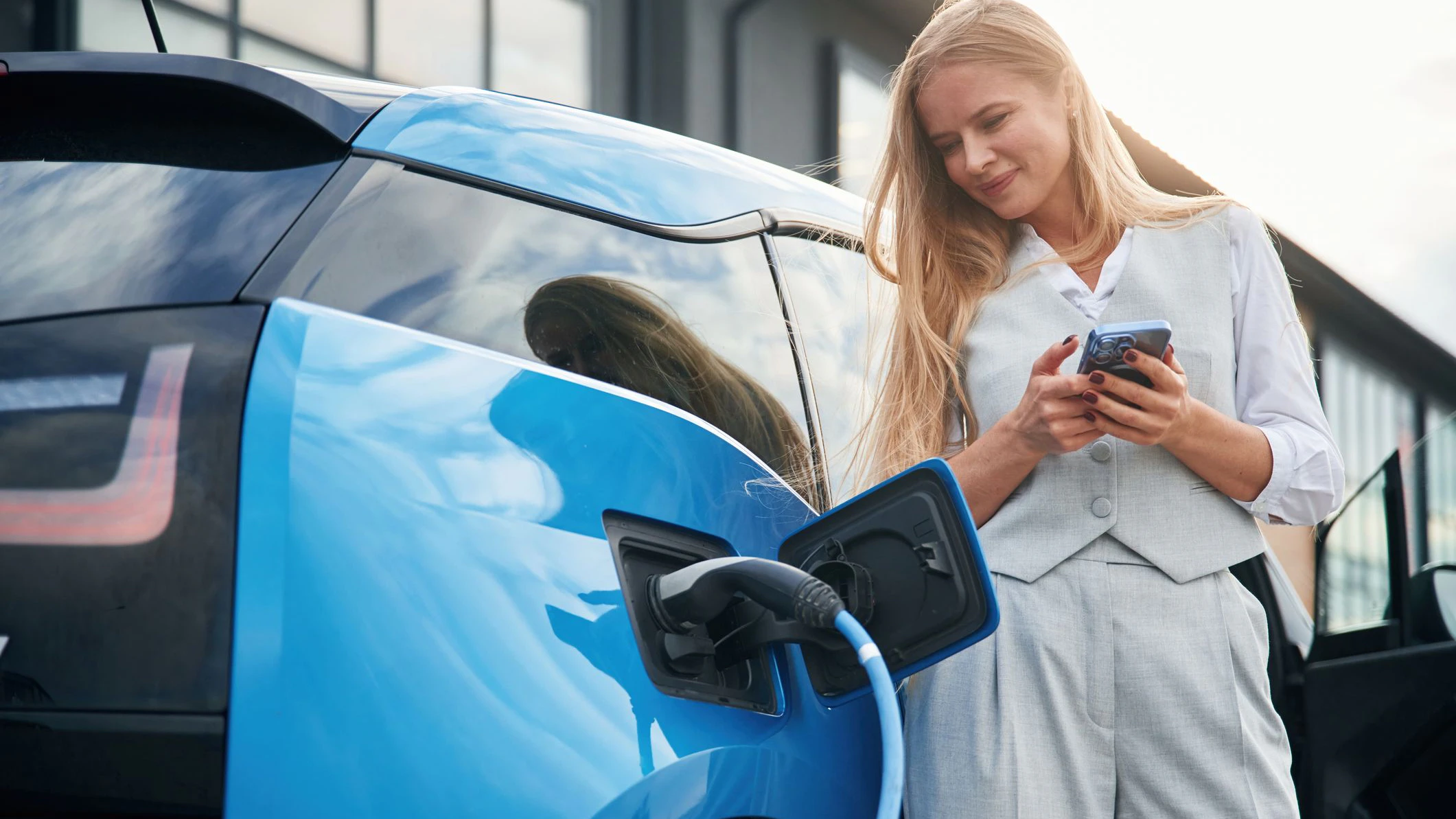Wire is in the socket. Woman on the electric cars charge station at daytime.
